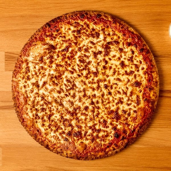 A large, round cheese pizza with a crispy crust and melted, bubbly cheese, next to a small cup of dipping sauce, on a wooden table.