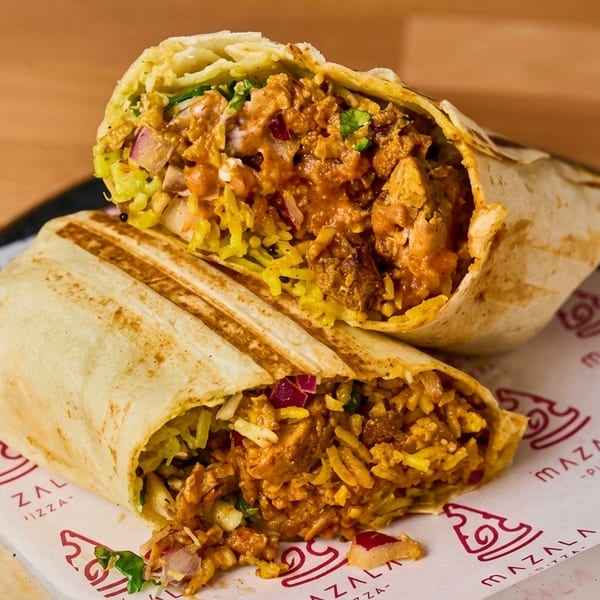 Two halves of a chicken tikka burrito, filled with rice, chicken, and red onions, on branded paper.