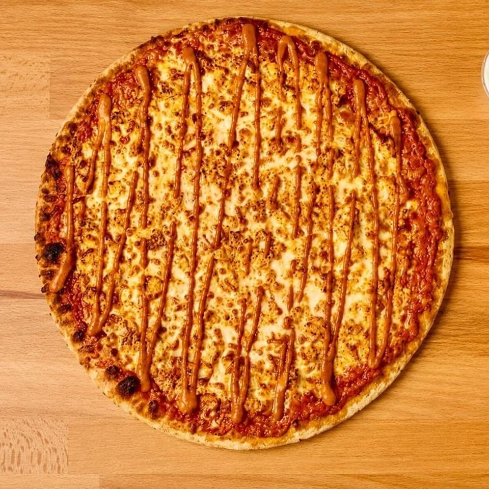Whole cheese pizza with a sauce drizzle and a side of white dipping sauce on a wooden table.