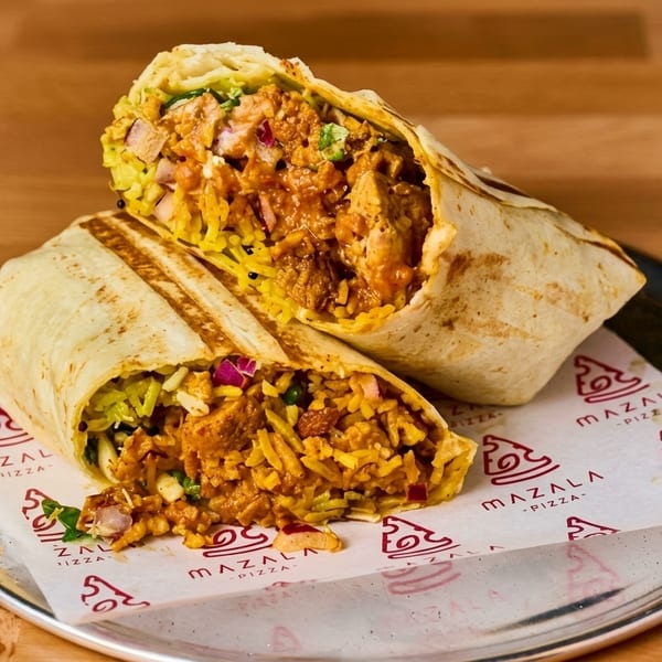 Two halves of a Mazala Pizza burrito, filled with yellow rice, chicken, and vegetables, on a metal plate.