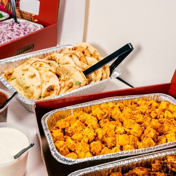Indian food catering with naan, paneer, chicken, sauces, and chopped vegetables in foil trays.