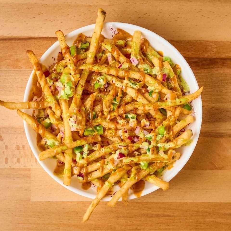 Loaded fries in a white bowl, topped with green and brown sauces, chopped onions, and peppers.